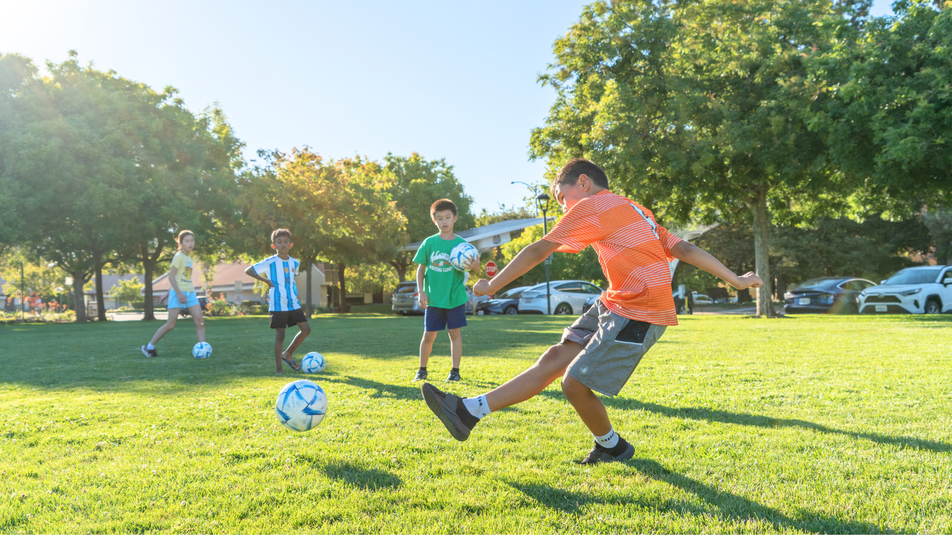 Children watch as a young participant kicks a blue FIFA soccer ball across Cupertino Library Field.