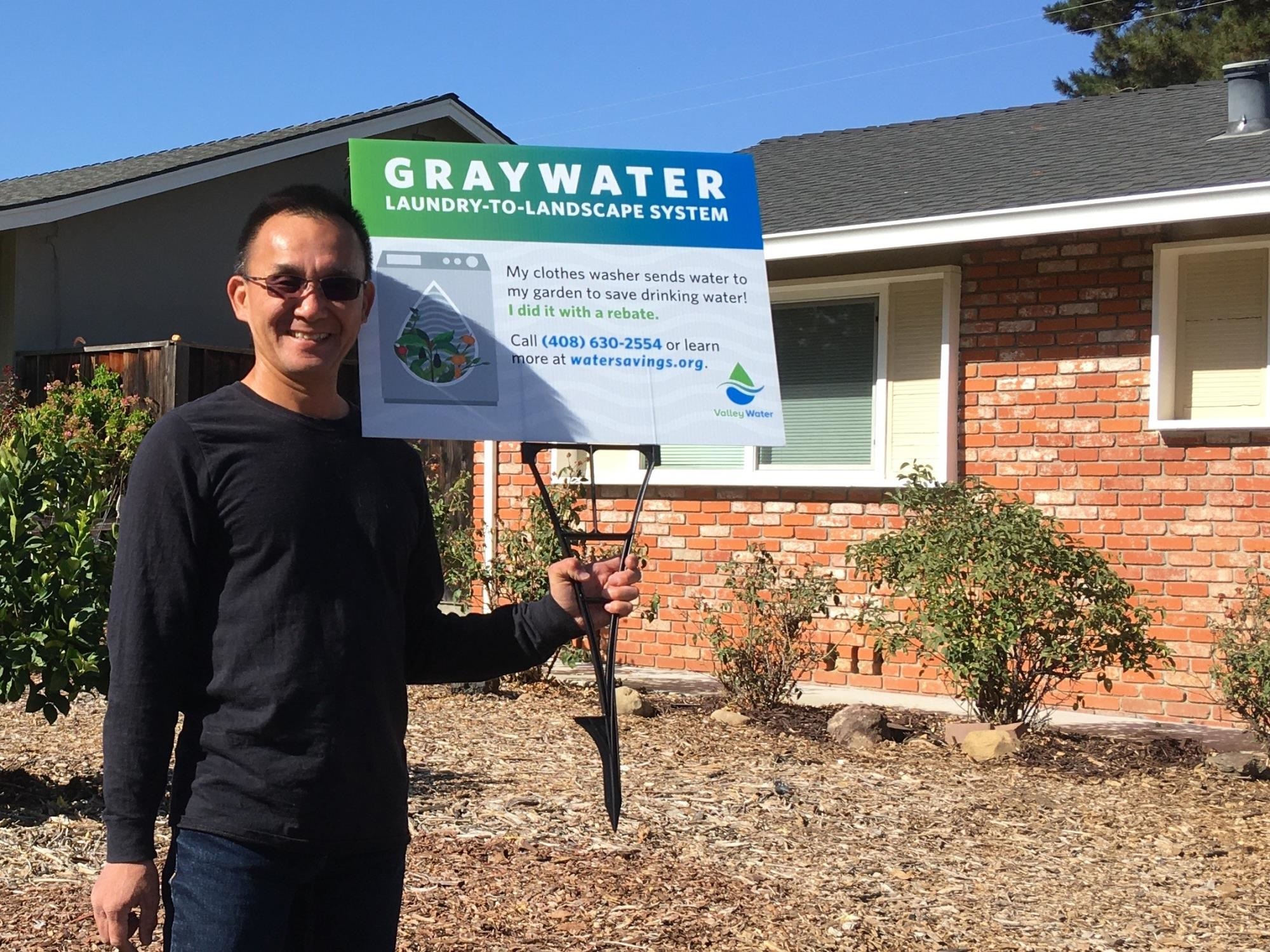 Man in front of home holding lawn sign for GrayWater rebate